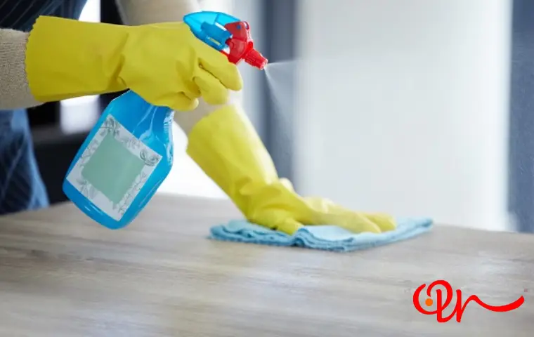 شخصی با دستکش در حال تمیز کردن سطح پارتیشن به کمک دستمال و اسپری تمیزکننده