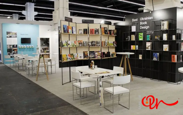 نمایشگاه کتاب شیراز با دکور و قفسه‌های مشکی و میز و صندلی سفید رنگ